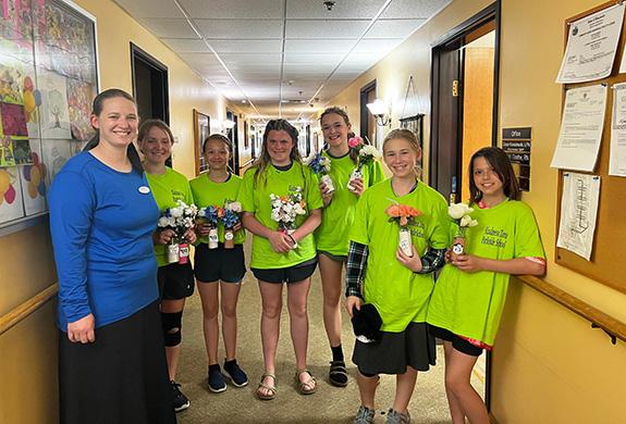 Camp Parkside Kindness Zone participants Sophie Klimke, Madelyn Reetz, Hannah Gunderson, Kelcey Michalski, Aralyn Wolsey, Lana Scott, visited Heartland House to deliver flowers to the residents on June 16. The group plans to make weekly stops to visit the residents throughout the next few weeks of Camp Parkside. Pictured with the group is Heartland House Activity Director Mindy Wolsey.