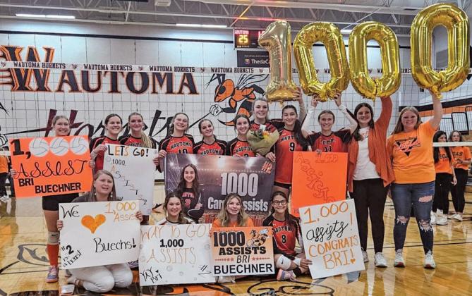 Wautoma Hornet, Brianna Buechner, proudly holds up her one-thousand assist banner surrounded by her teammates..