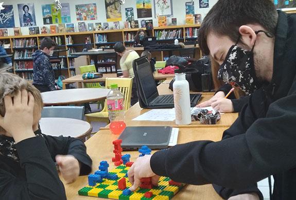 Ethan Gumz, and eleventh grader A+ Program Assistant, plays a game of chess during academic time with Chase Caswell, fourth grader, on a chessboard Chase made in Lego club.