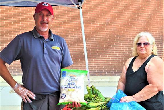 Vendor Travis Cernoch, Daytona Beach, FL, just completed a sale of sea food to Julie Tomasko, Wautoma.  He was also giving free sweet corn to his customers.  Cernoch said he has been coming to Wautoma for the last four or five years and loves coming to Wautoma, stating Wautoma is like his second home.  He said he is grateful for the support he has received in the Wautoma community.